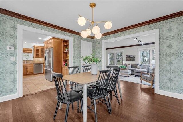 dining space with crown molding, sink, an inviting chandelier, and light wood-type flooring