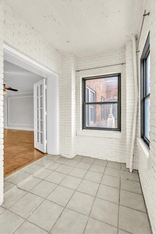 tiled spare room featuring ceiling fan and brick wall