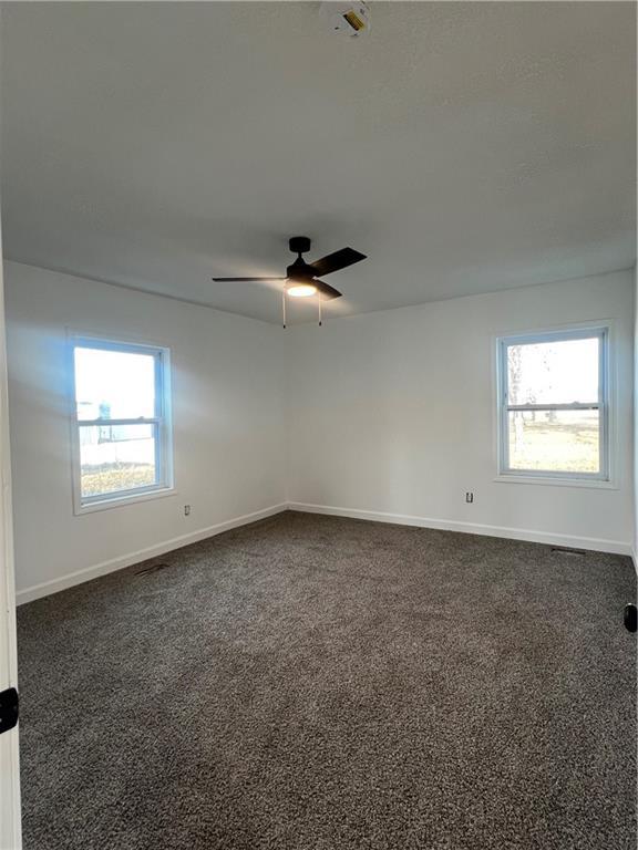 unfurnished room with ceiling fan, dark carpet, and a healthy amount of sunlight