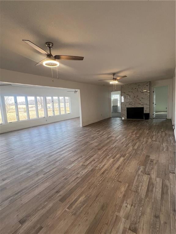 unfurnished living room featuring wood-type flooring, a stone fireplace, and a healthy amount of sunlight