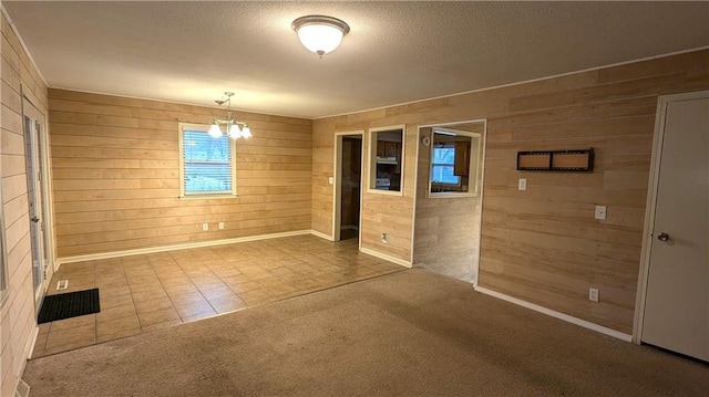 spare room with carpet, an inviting chandelier, a textured ceiling, and wooden walls