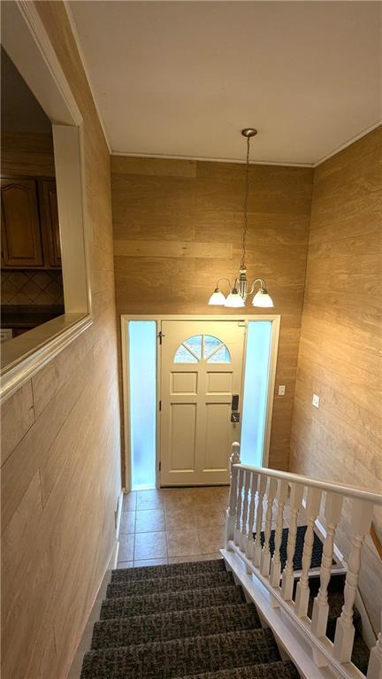 stairs with tile patterned flooring, a chandelier, and wood walls