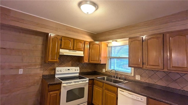 kitchen featuring white appliances, wood walls, sink, and backsplash