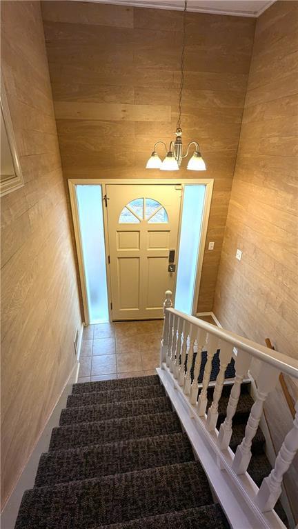 stairway featuring tile patterned flooring, a notable chandelier, and wood walls