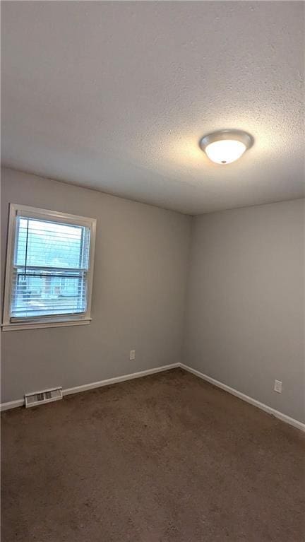 empty room with a textured ceiling and dark colored carpet