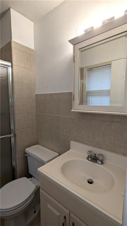 bathroom featuring toilet, a shower with shower door, a textured ceiling, tile walls, and vanity