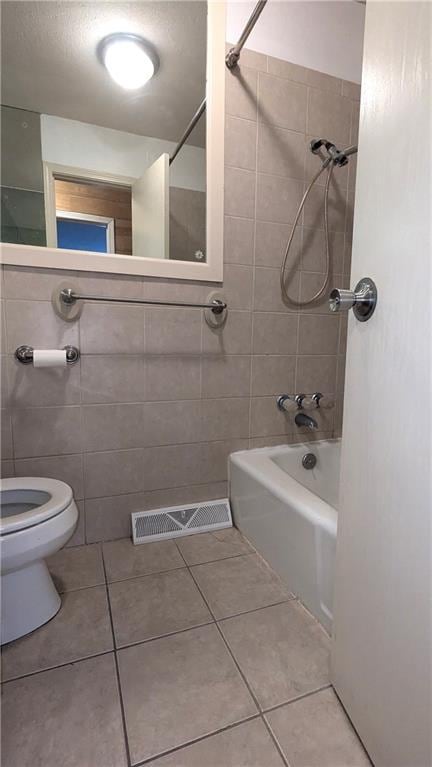 bathroom featuring tiled shower / bath combo, tile walls, tile patterned floors, and toilet