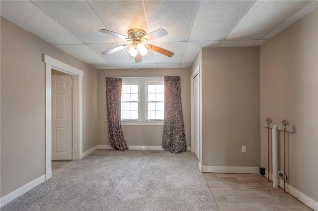 empty room with a drop ceiling, light colored carpet, and ceiling fan