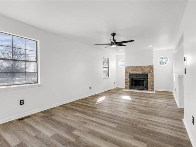 unfurnished living room featuring ceiling fan, a fireplace, light hardwood / wood-style flooring, and a wealth of natural light