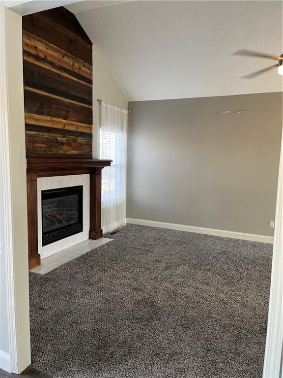 unfurnished living room featuring light carpet, vaulted ceiling, a tile fireplace, and ceiling fan