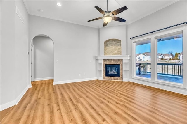 unfurnished living room with ceiling fan, ornamental molding, a tiled fireplace, and light hardwood / wood-style flooring