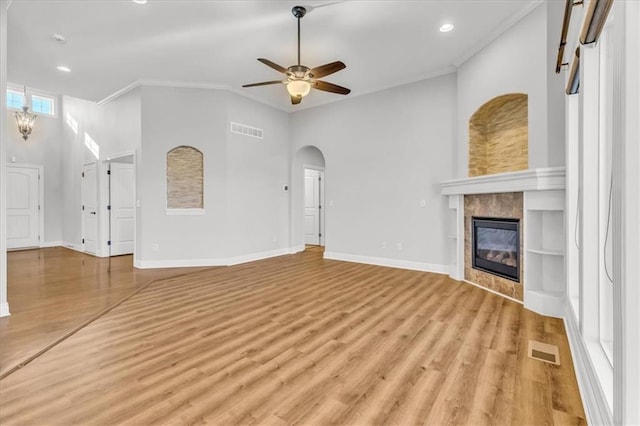 unfurnished living room with ornamental molding, ceiling fan with notable chandelier, a fireplace, and light hardwood / wood-style floors