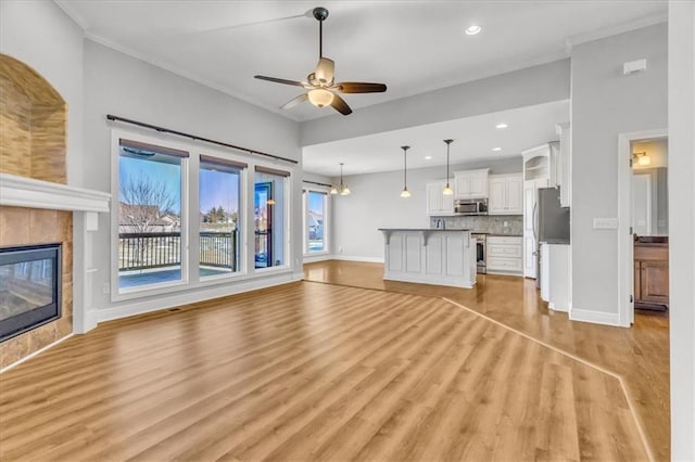 unfurnished living room featuring crown molding, a tile fireplace, light hardwood / wood-style floors, and ceiling fan