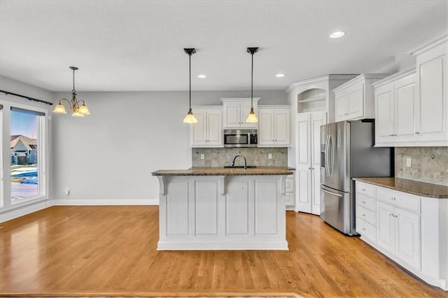 kitchen featuring white cabinetry, a kitchen breakfast bar, an island with sink, pendant lighting, and stainless steel appliances