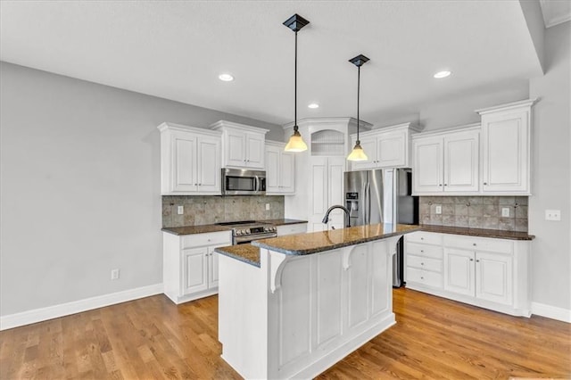 kitchen with pendant lighting, a breakfast bar, white cabinetry, stainless steel appliances, and an island with sink