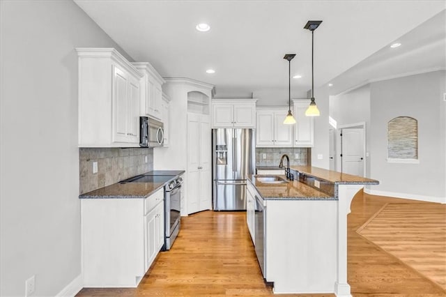 kitchen with sink, hanging light fixtures, stainless steel appliances, white cabinets, and dark stone counters