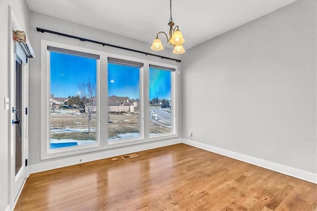 unfurnished dining area with hardwood / wood-style flooring, a healthy amount of sunlight, and a notable chandelier