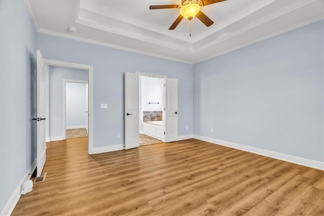 unfurnished bedroom featuring ensuite bathroom, ornamental molding, ceiling fan, a raised ceiling, and light wood-type flooring