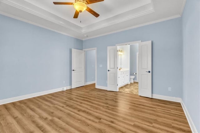 unfurnished bedroom with connected bathroom, a tray ceiling, light hardwood / wood-style flooring, and ornamental molding