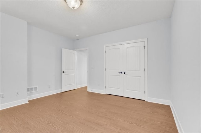 unfurnished bedroom featuring a textured ceiling, light wood-type flooring, and a closet