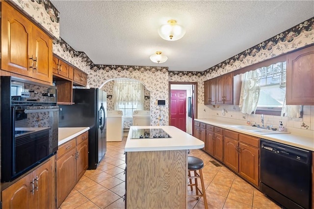 kitchen featuring wallpapered walls, a center island, washing machine and clothes dryer, black appliances, and a sink