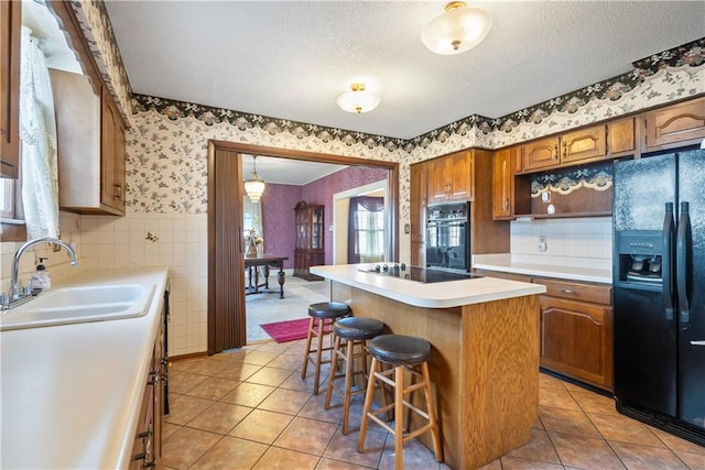 kitchen with light tile patterned flooring, a kitchen island, sink, a breakfast bar area, and black appliances