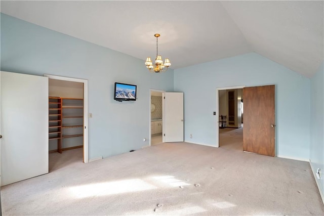 unfurnished bedroom featuring a chandelier, ensuite bathroom, carpet flooring, vaulted ceiling, and a walk in closet