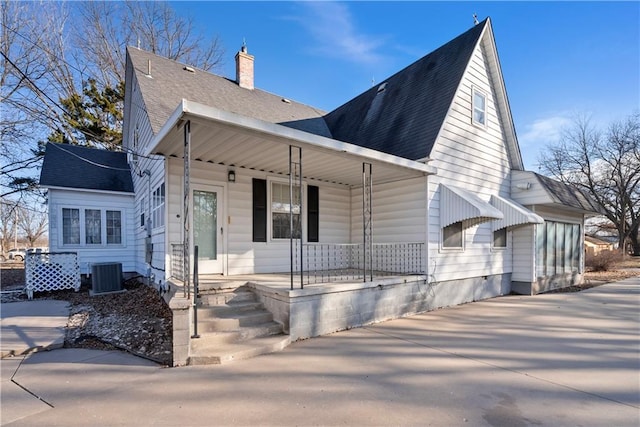 view of front facade with a shingled roof, cooling unit, covered porch, and a chimney