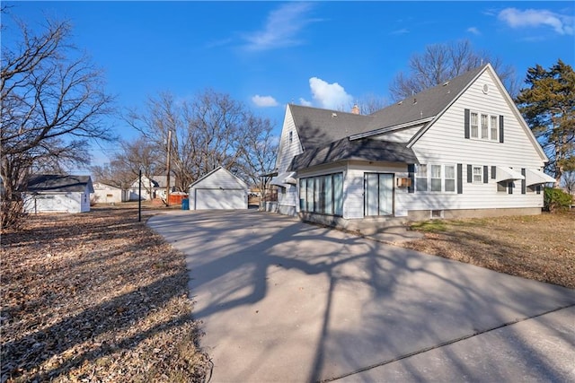 view of home's exterior with roof with shingles, a detached garage, a chimney, an outdoor structure, and driveway