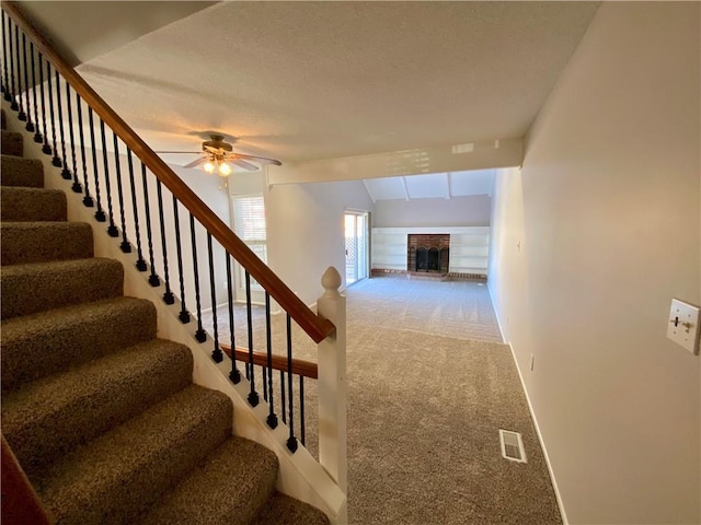 stairway featuring ceiling fan, a brick fireplace, and carpet