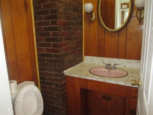 bathroom featuring vanity, toilet, and brick wall