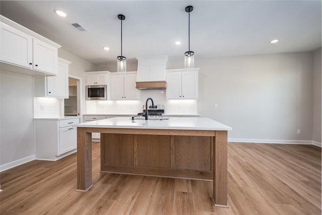 kitchen with white cabinetry, appliances with stainless steel finishes, decorative light fixtures, and an island with sink