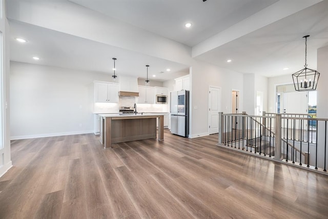 kitchen with white cabinetry, hanging light fixtures, hardwood / wood-style floors, stainless steel appliances, and an island with sink