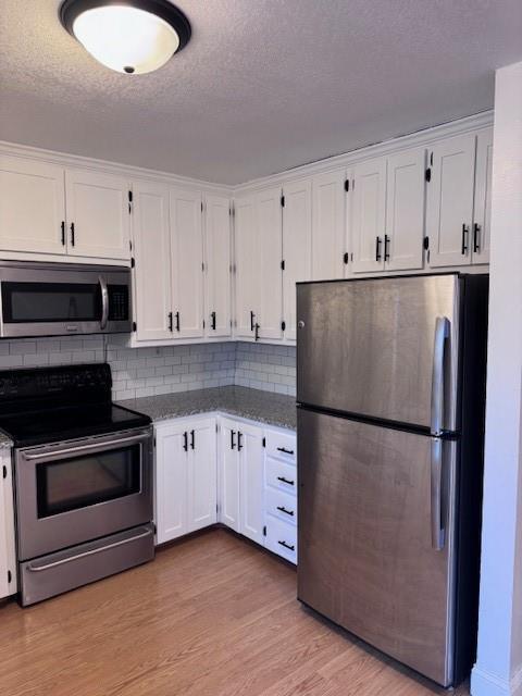 kitchen featuring light hardwood / wood-style flooring, stainless steel appliances, tasteful backsplash, light stone countertops, and white cabinets