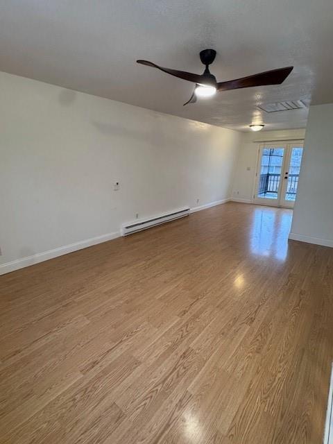 unfurnished room featuring baseboard heating, ceiling fan, and light hardwood / wood-style floors