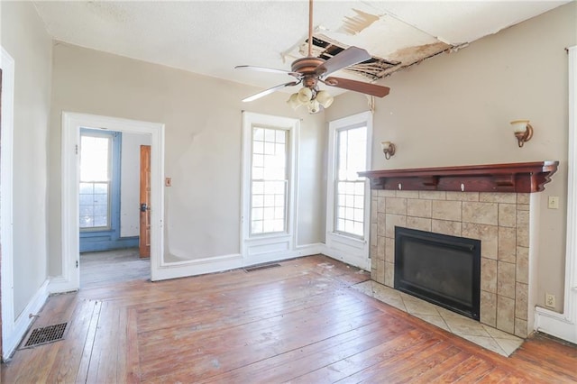 unfurnished living room featuring a tiled fireplace, light hardwood / wood-style flooring, and ceiling fan