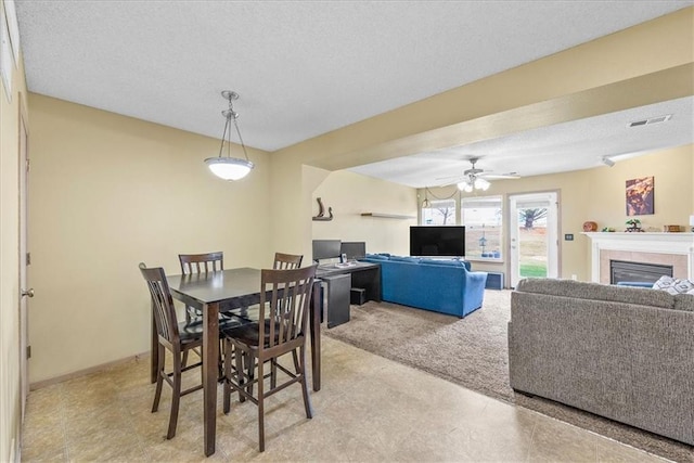 dining room with a textured ceiling, a tile fireplace, visible vents, and a ceiling fan