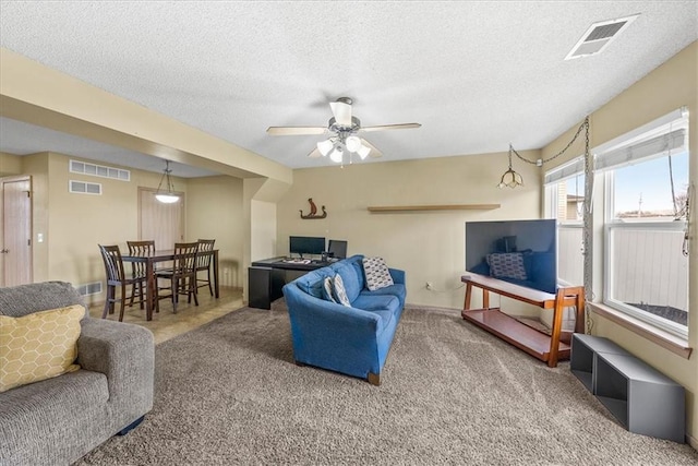 carpeted living room featuring a ceiling fan, visible vents, and a textured ceiling