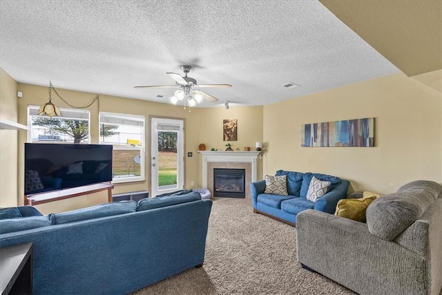 living room featuring ceiling fan, a glass covered fireplace, a textured ceiling, and carpet flooring