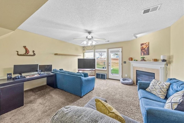 living area with carpet, visible vents, a tiled fireplace, ceiling fan, and a textured ceiling