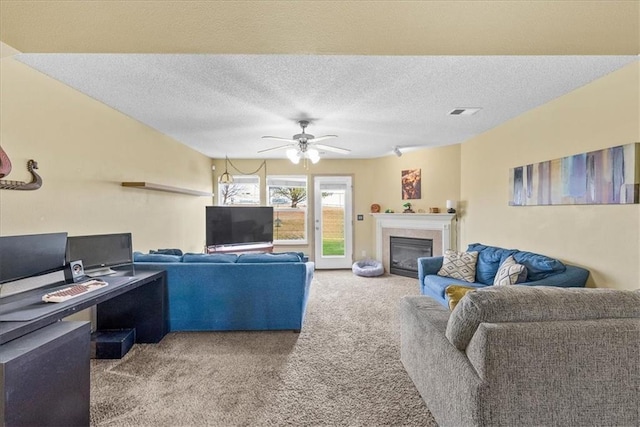 carpeted living area featuring a textured ceiling, a glass covered fireplace, visible vents, and a ceiling fan