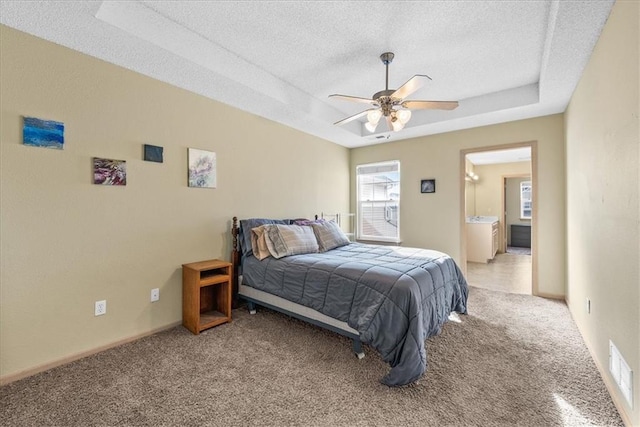 carpeted bedroom featuring a textured ceiling, ceiling fan, visible vents, baseboards, and a tray ceiling