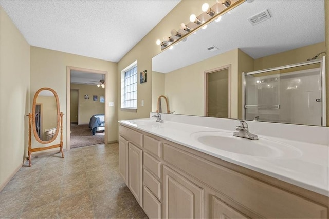 bathroom featuring double vanity, a stall shower, visible vents, a textured ceiling, and a sink