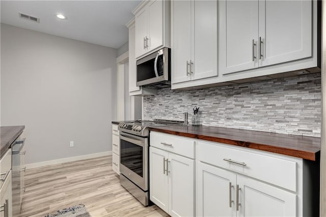 kitchen featuring visible vents, wooden counters, decorative backsplash, appliances with stainless steel finishes, and baseboards