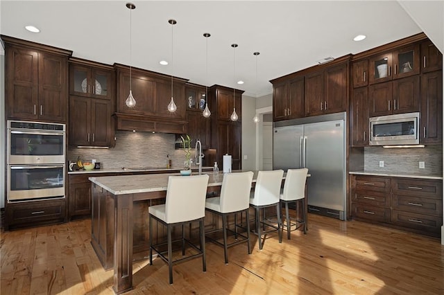 kitchen featuring tasteful backsplash, a kitchen breakfast bar, light wood finished floors, and built in appliances