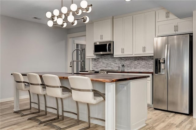 kitchen featuring visible vents, an island with sink, appliances with stainless steel finishes, wooden counters, and backsplash