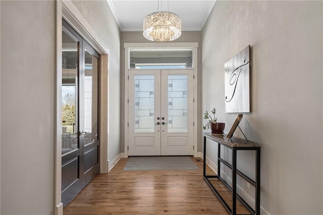 entryway featuring french doors, crown molding, wood finished floors, a chandelier, and baseboards