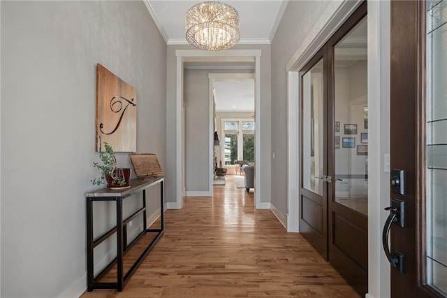 hallway with light wood-style floors, a notable chandelier, ornamental molding, and baseboards