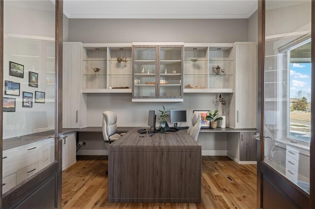 office with light wood finished floors, built in desk, and crown molding