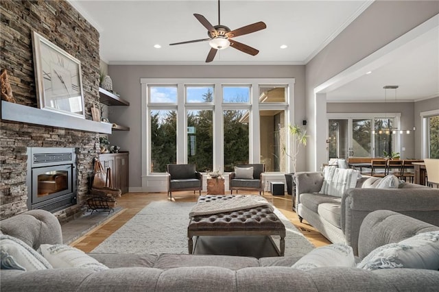 living area featuring a stone fireplace, recessed lighting, wood finished floors, a ceiling fan, and crown molding